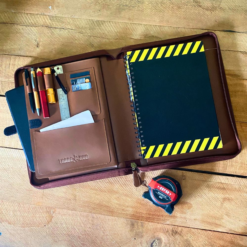 Open leather work folder showing tools, ruler, pens, and spiral notepad with yellow safety stripes