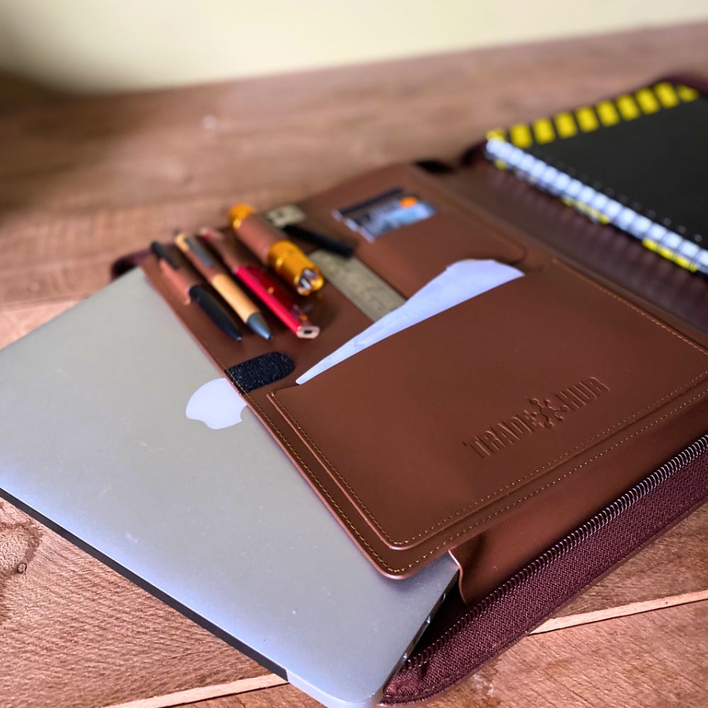 Open leather folder with tools and MacBook partially inserted, displayed on timber surface