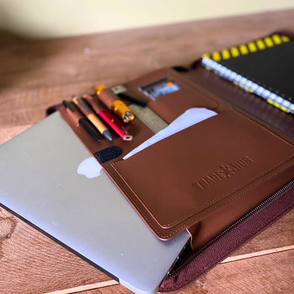 Open leather folder with tools and MacBook partially inserted, displayed on timber surface