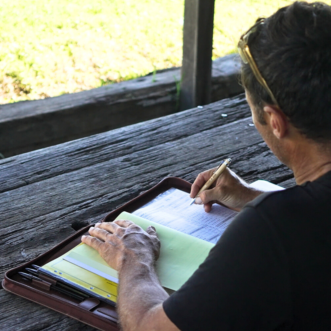 TradeHub compendium open on outdoor timber table with paperwork being filled out